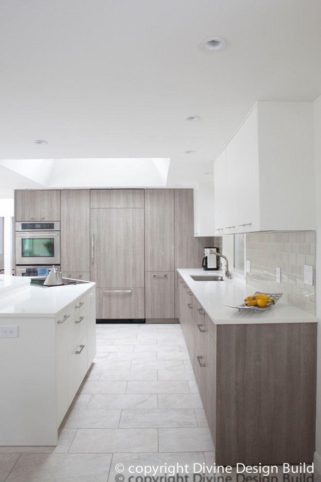 Modern inredning av ett kök, med en undermonterad diskho, släta luckor, grå skåp, grått stänkskydd, stänkskydd i tunnelbanekakel, rostfria vitvaror, klinkergolv i porslin och en köksö