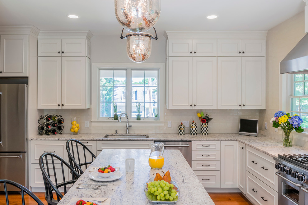 Photo of a large traditional kitchen in Boston with white cabinets, granite worktops, white splashback, ceramic splashback, stainless steel appliances, medium hardwood flooring and an island.