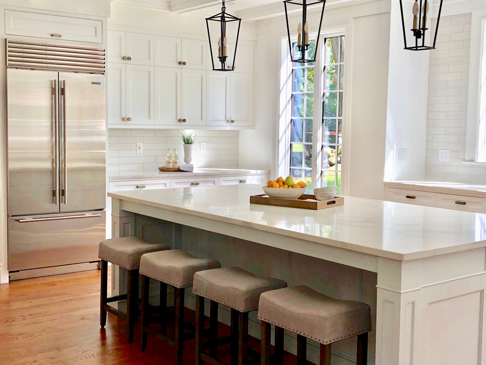 Large transitional u-shaped light wood floor and beige floor eat-in kitchen photo with an undermount sink, recessed-panel cabinets, white cabinets, quartz countertops, white backsplash, ceramic backsplash, stainless steel appliances, an island and white countertops