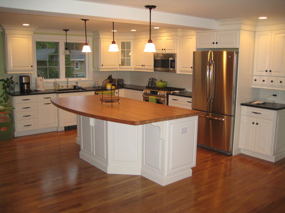 Example of a mid-sized classic l-shaped medium tone wood floor eat-in kitchen design in Boston with an undermount sink, raised-panel cabinets, white cabinets, granite countertops, white backsplash, subway tile backsplash and stainless steel appliances