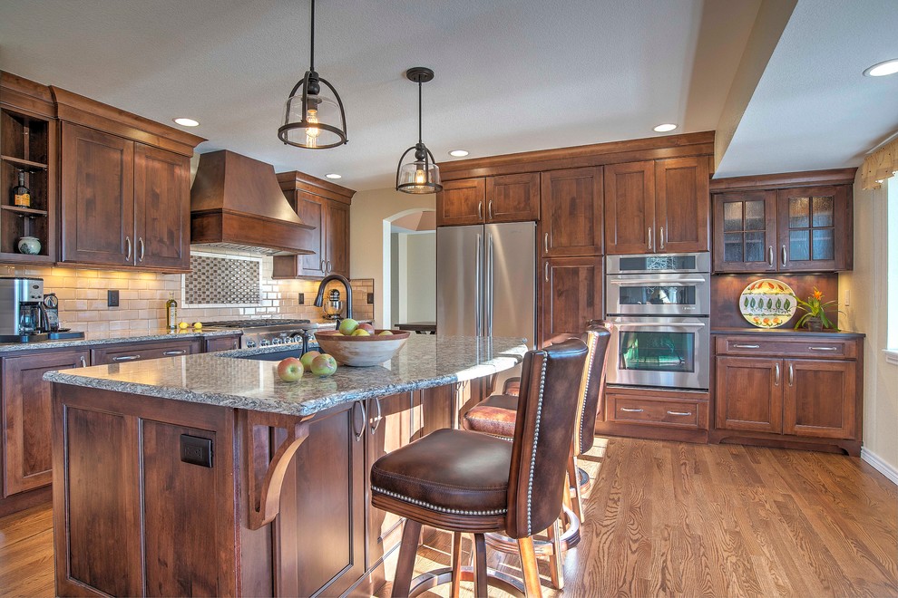 Design ideas for a large traditional l-shaped kitchen in Denver with a submerged sink, shaker cabinets, medium wood cabinets, engineered stone countertops, beige splashback, metro tiled splashback, medium hardwood flooring and an island.