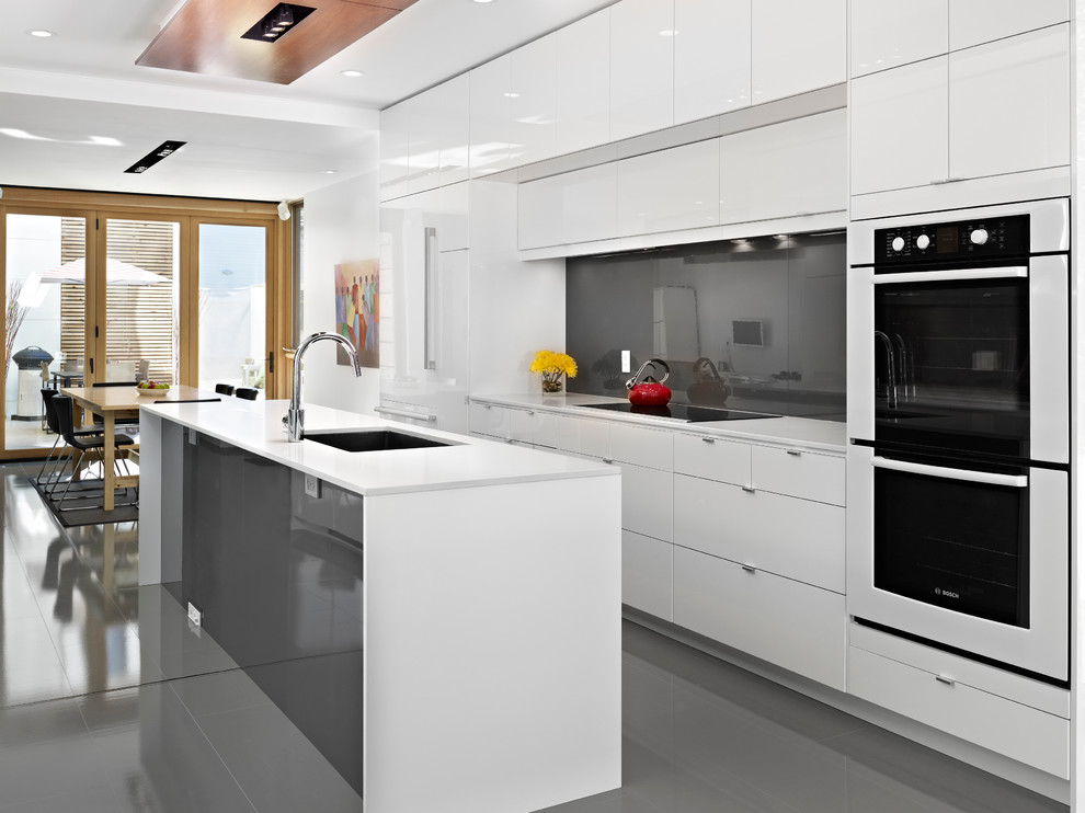 Bild på ett stort funkis kök, med en undermonterad diskho, släta luckor, vita skåp, bänkskiva i kvarts, grått stänkskydd, stänkskydd i sten, vita vitvaror, klinkergolv i porslin, en köksö och grått golv