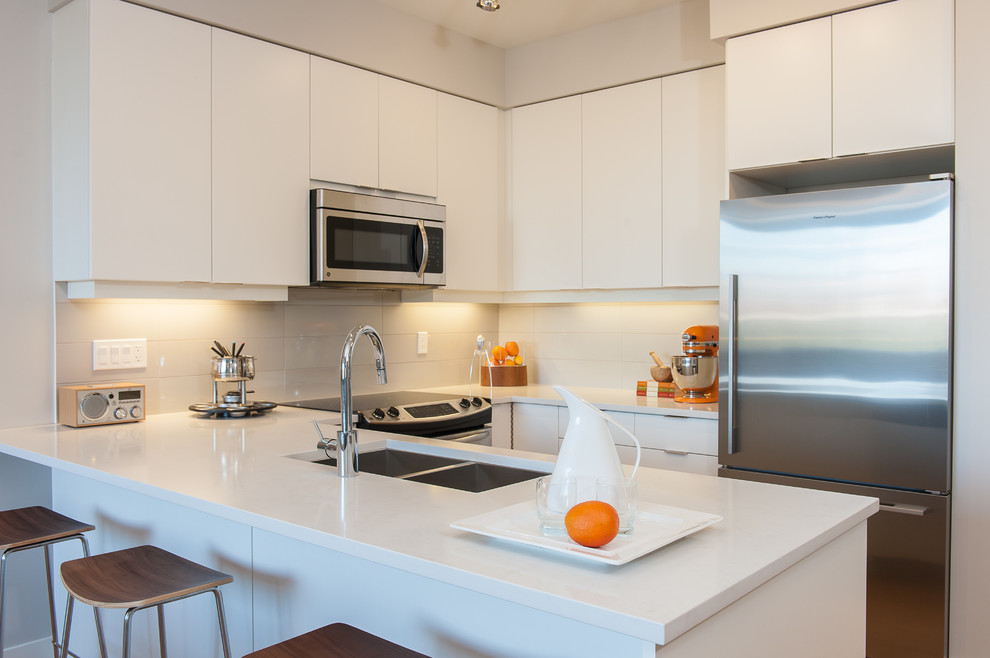 Example of a small minimalist u-shaped light wood floor open concept kitchen design in Vancouver with an undermount sink, flat-panel cabinets, white cabinets, quartz countertops, gray backsplash, porcelain backsplash, stainless steel appliances and a peninsula