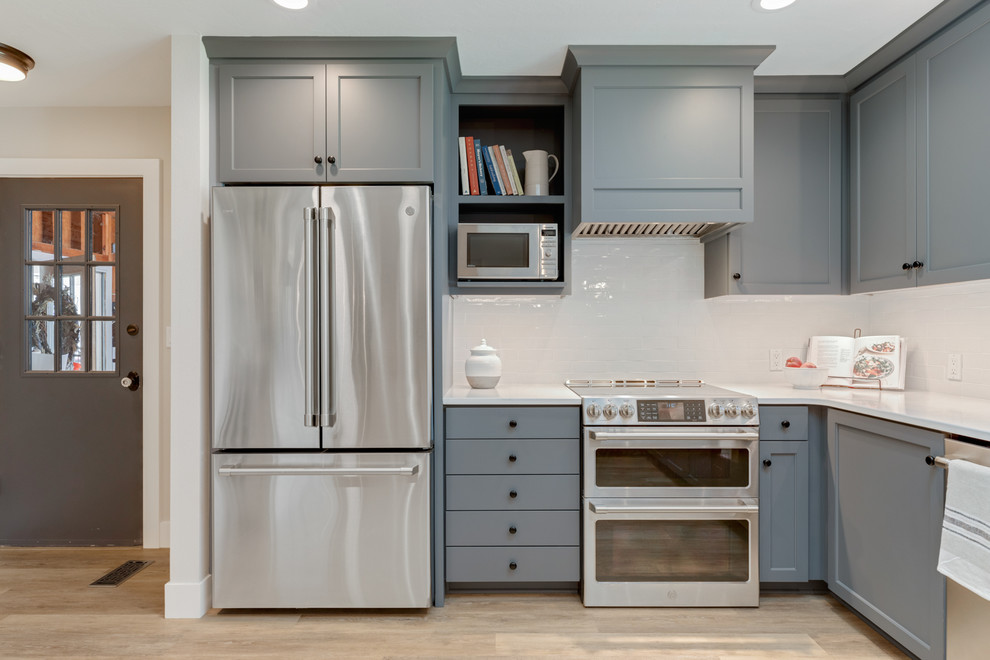 Landhausstil Küche mit Landhausspüle, grauen Schränken, Küchenrückwand in Weiß, Küchengeräten aus Edelstahl und weißer Arbeitsplatte