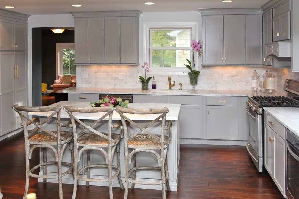 Foto på ett kök, med grå skåp, beige stänkskydd, rostfria vitvaror, mörkt trägolv och en köksö