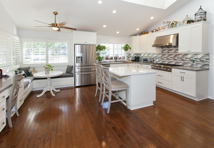 Foto på ett funkis kök, med luckor med infälld panel, vita skåp, flerfärgad stänkskydd, stänkskydd i stickkakel, rostfria vitvaror, mellanmörkt trägolv och en köksö