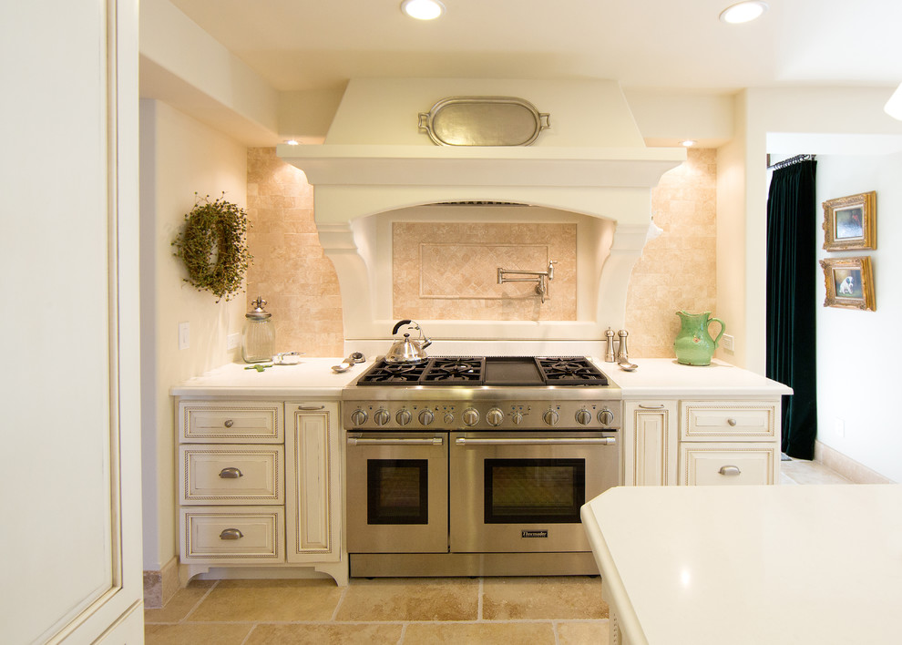 Ejemplo de cocina mediterránea con armarios con paneles con relieve, puertas de armario blancas, salpicadero beige y electrodomésticos de acero inoxidable