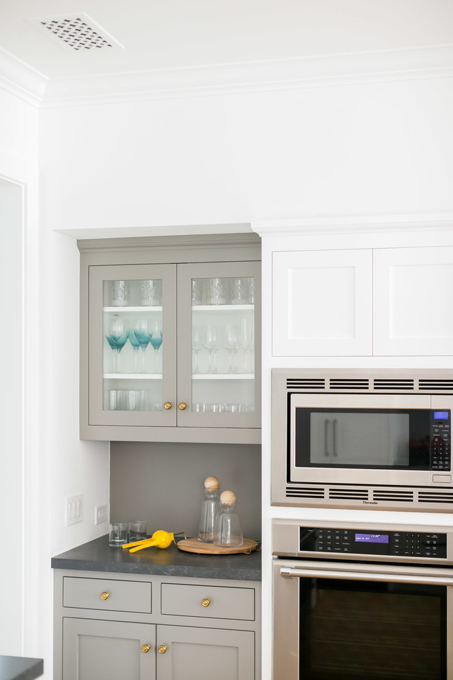 Example of a mid-sized beach style l-shaped light wood floor eat-in kitchen design in Orange County with white cabinets, white backsplash, stainless steel appliances and an island