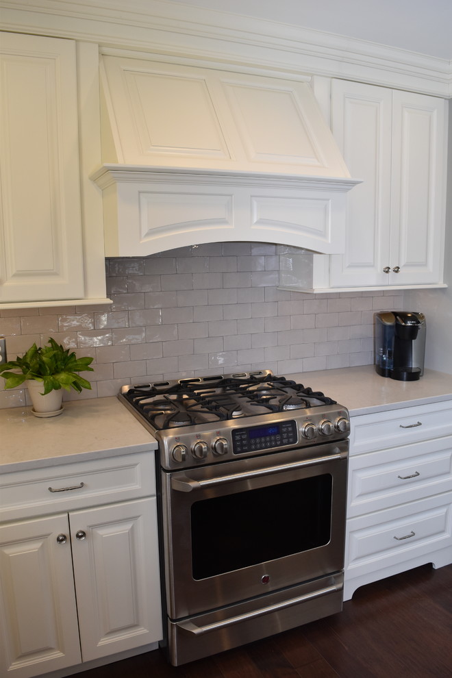 Inredning av ett klassiskt mellanstort kök, med en undermonterad diskho, luckor med upphöjd panel, vita skåp, bänkskiva i kvarts, grått stänkskydd, stänkskydd i keramik, rostfria vitvaror, mörkt trägolv och en köksö