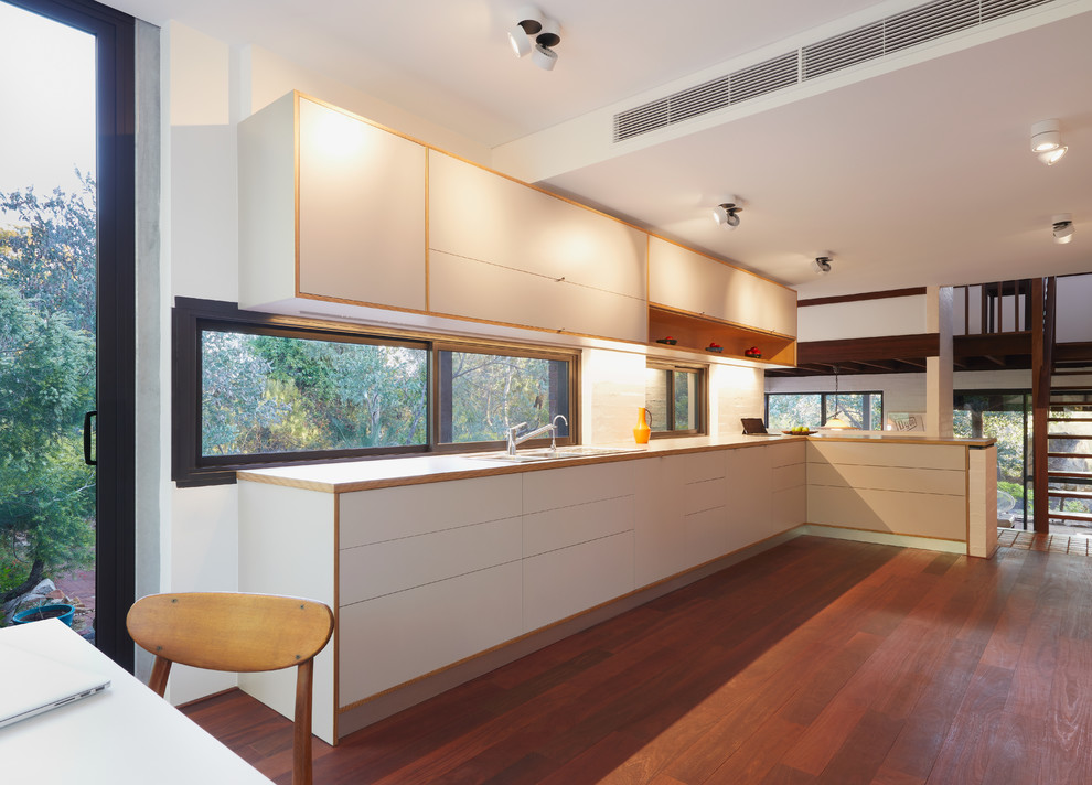 Mittelgroße Moderne Wohnküche in L-Form mit Doppelwaschbecken, weißen Schränken, Laminat-Arbeitsplatte, Rückwand-Fenster, Küchengeräten aus Edelstahl, dunklem Holzboden und rotem Boden in Perth