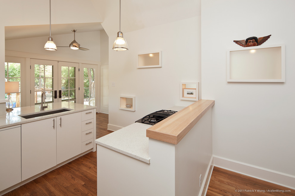 Example of a trendy l-shaped medium tone wood floor eat-in kitchen design in Austin with an undermount sink, flat-panel cabinets, white cabinets, quartz countertops, white backsplash, mosaic tile backsplash, stainless steel appliances and a peninsula