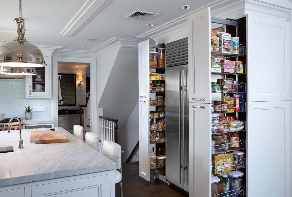 Large classic l-shaped kitchen pantry in New York with a submerged sink, glass-front cabinets, white cabinets, marble worktops, white splashback, glass tiled splashback, stainless steel appliances, dark hardwood flooring and an island.