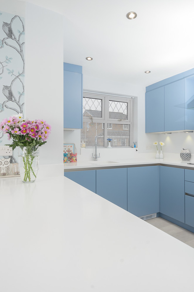 Idee per una cucina moderna di medie dimensioni con lavello integrato, ante lisce, ante blu, top in superficie solida, paraspruzzi bianco, elettrodomestici da incasso, pavimento in linoleum e penisola