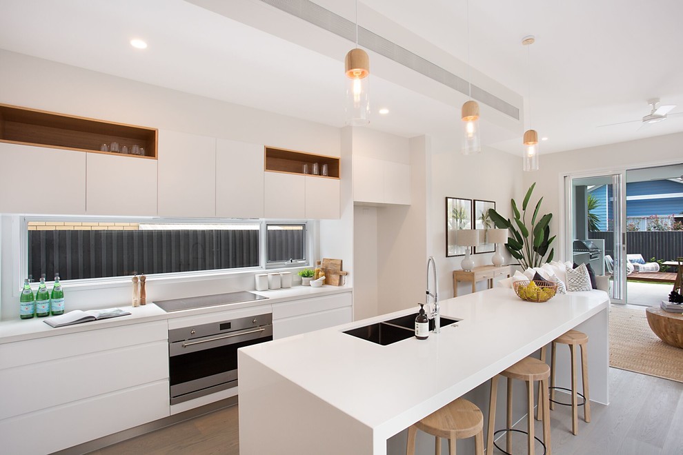Foto di una cucina design con lavello sottopiano, ante bianche, elettrodomestici in acciaio inossidabile, parquet chiaro, pavimento marrone e top bianco