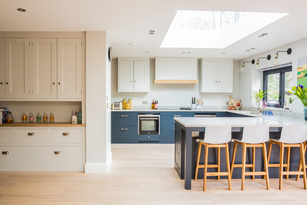 This is an example of a large contemporary u-shaped open plan kitchen in London with a double-bowl sink, shaker cabinets, engineered stone countertops, integrated appliances, blue cabinets and a breakfast bar.