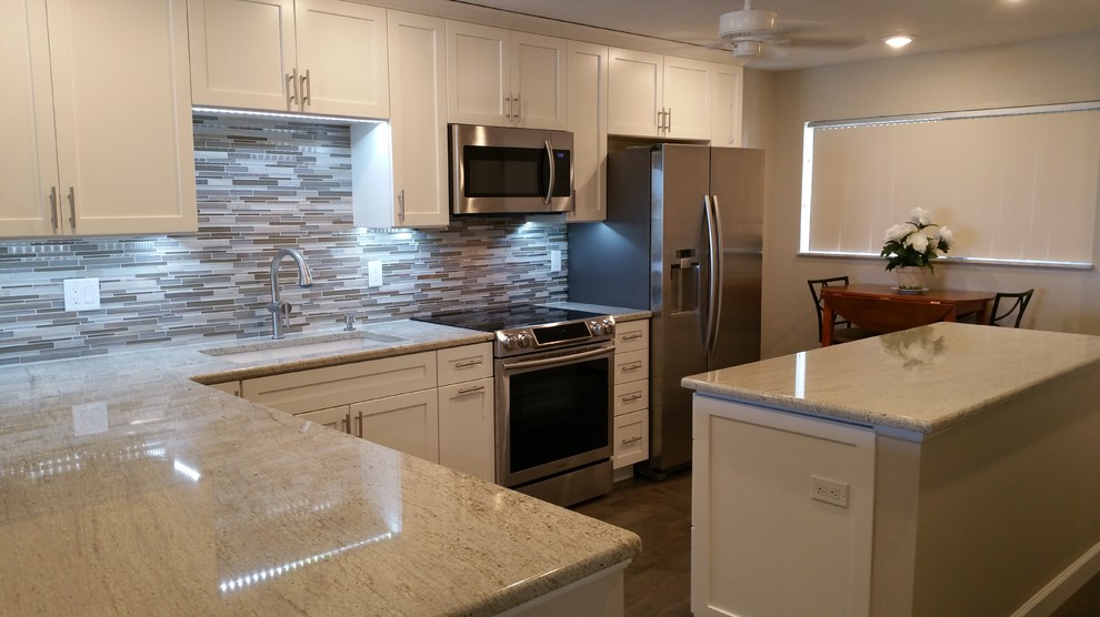 Medium sized nautical l-shaped open plan kitchen in Tampa with a submerged sink, shaker cabinets, white cabinets, granite worktops, multi-coloured splashback, mosaic tiled splashback, stainless steel appliances, medium hardwood flooring and an island.