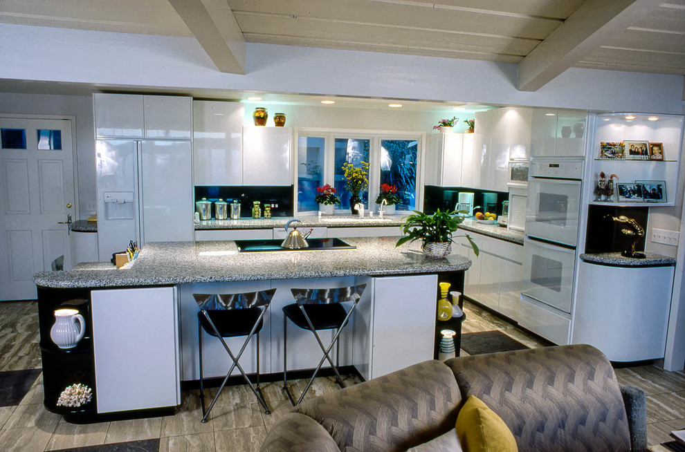 Foto på ett mycket stort retro kök, med en undermonterad diskho, släta luckor, vita skåp, granitbänkskiva, svart stänkskydd, stänkskydd i sten, vita vitvaror, marmorgolv och en köksö