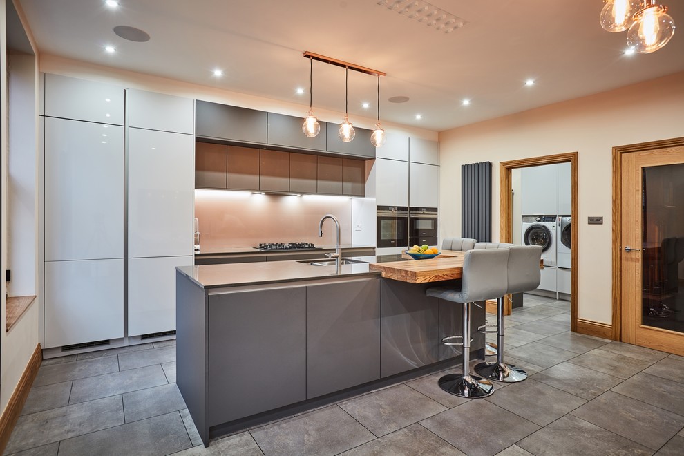 Inspiration for a medium sized modern single-wall kitchen/diner in Other with a built-in sink, flat-panel cabinets, grey cabinets, quartz worktops, metallic splashback, glass sheet splashback, stainless steel appliances, ceramic flooring, an island, grey floors and grey worktops.