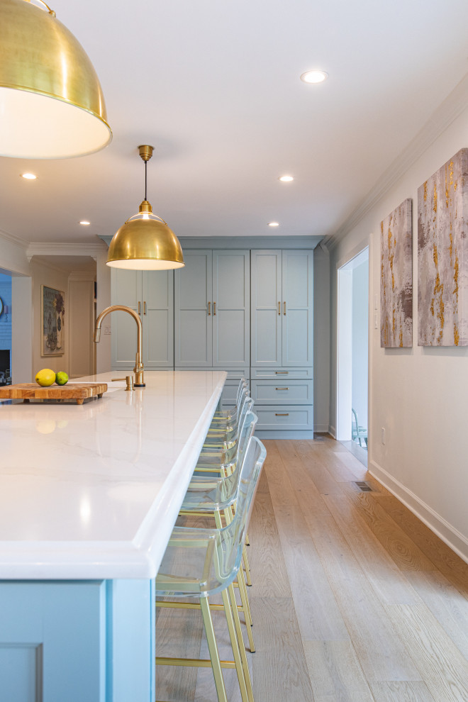 Foto på ett stort lantligt vit kök, med en rustik diskho, luckor med infälld panel, blå skåp, bänkskiva i kvarts, vitt stänkskydd, rostfria vitvaror, ljust trägolv, en köksö och beiget golv