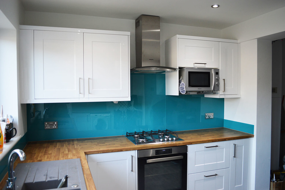 Modern inredning av ett stort kök och matrum, med släta luckor, vita skåp, träbänkskiva, blått stänkskydd och glaspanel som stänkskydd