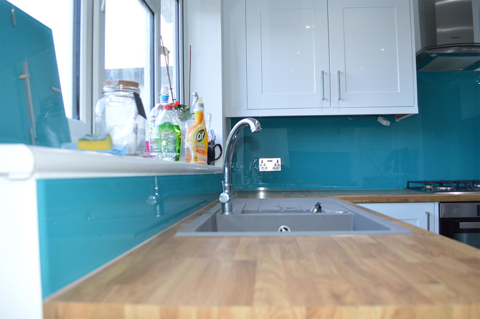 Immagine di una grande cucina abitabile minimalista con ante lisce, ante bianche, top in legno, paraspruzzi blu, paraspruzzi con lastra di vetro e nessuna isola