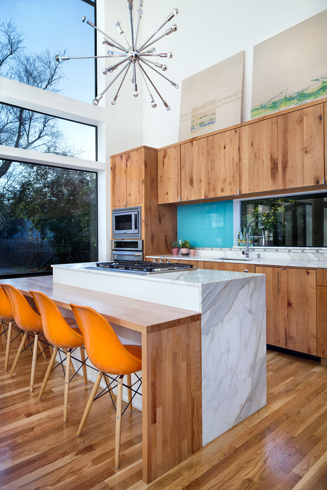 Modern inredning av ett mellanstort kök, med en undermonterad diskho, släta luckor, skåp i mellenmörkt trä, granitbänkskiva, blått stänkskydd, glaspanel som stänkskydd, rostfria vitvaror, mellanmörkt trägolv och en köksö