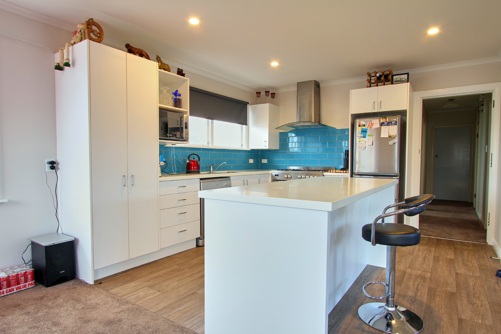 Mittelgroße Moderne Wohnküche in L-Form mit Küchenrückwand in Blau, Rückwand aus Keramikfliesen, Küchengeräten aus Edelstahl, Kücheninsel, braunem Boden und weißer Arbeitsplatte in Sonstige
