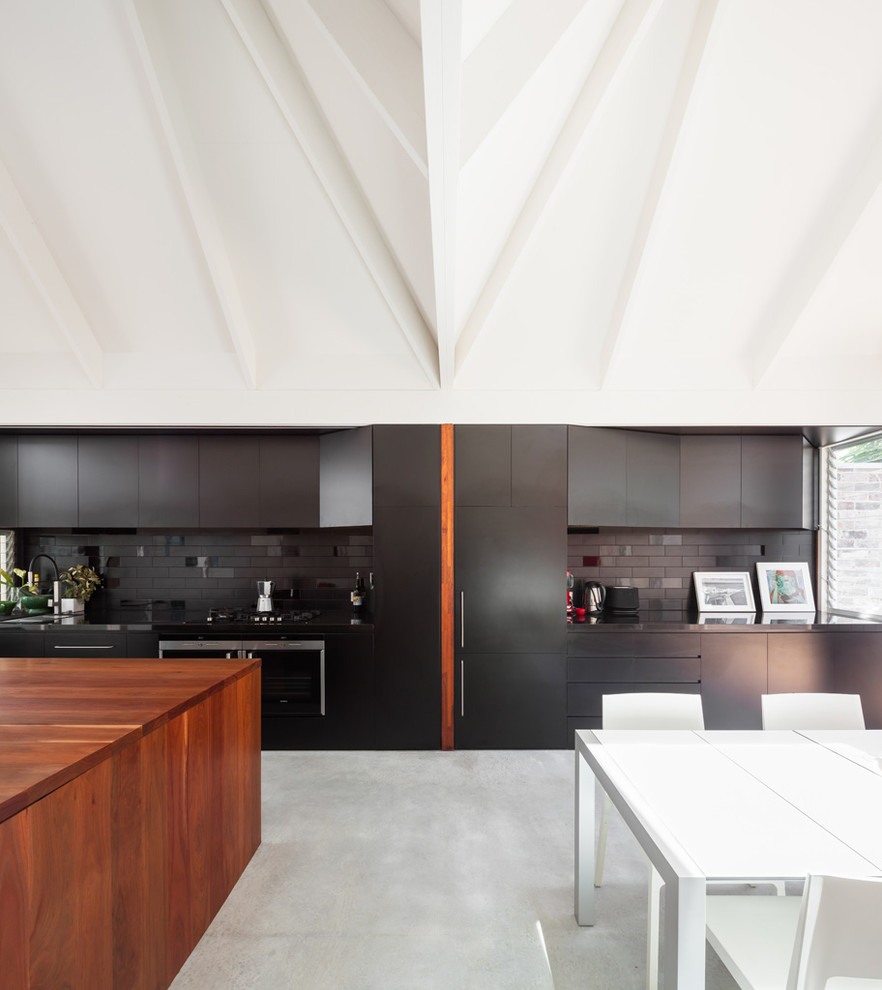 На фото: большая кухня в современном стиле с плоскими фасадами, черными фасадами, черным фартуком и бетонным полом с