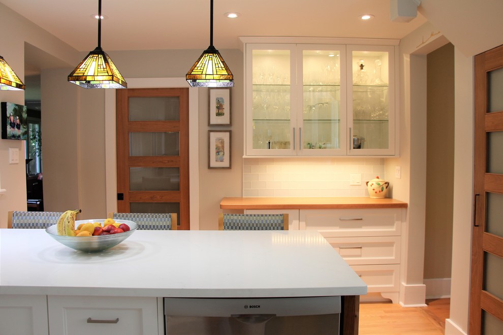 Inspiration for a medium sized contemporary u-shaped kitchen in Ottawa with a submerged sink, glass-front cabinets, white cabinets, engineered stone countertops, white splashback, glass tiled splashback, stainless steel appliances, medium hardwood flooring, a breakfast bar and white worktops.