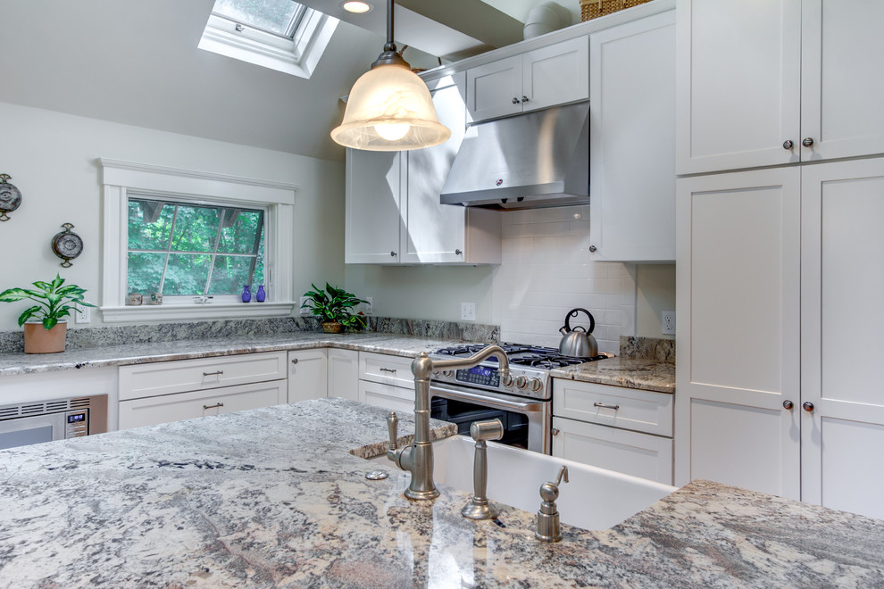 Large elegant l-shaped light wood floor eat-in kitchen photo in Boston with a farmhouse sink, shaker cabinets, white cabinets, granite countertops, white backsplash, subway tile backsplash, stainless steel appliances and an island