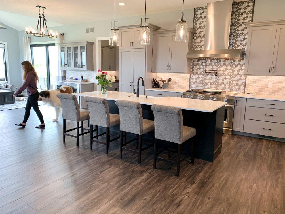 Large cottage l-shaped vinyl floor and brown floor open concept kitchen photo in Other with a farmhouse sink, flat-panel cabinets, gray cabinets, quartz countertops, metallic backsplash, metal backsplash, stainless steel appliances, an island and white countertops