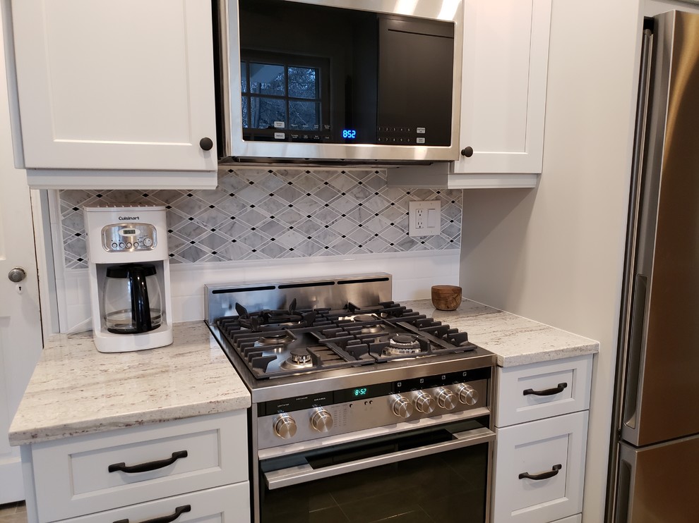 Photo of a small classic galley kitchen pantry in New York with a belfast sink, shaker cabinets, grey cabinets, granite worktops, black splashback, marble splashback, stainless steel appliances, porcelain flooring, no island, grey floors and white worktops.