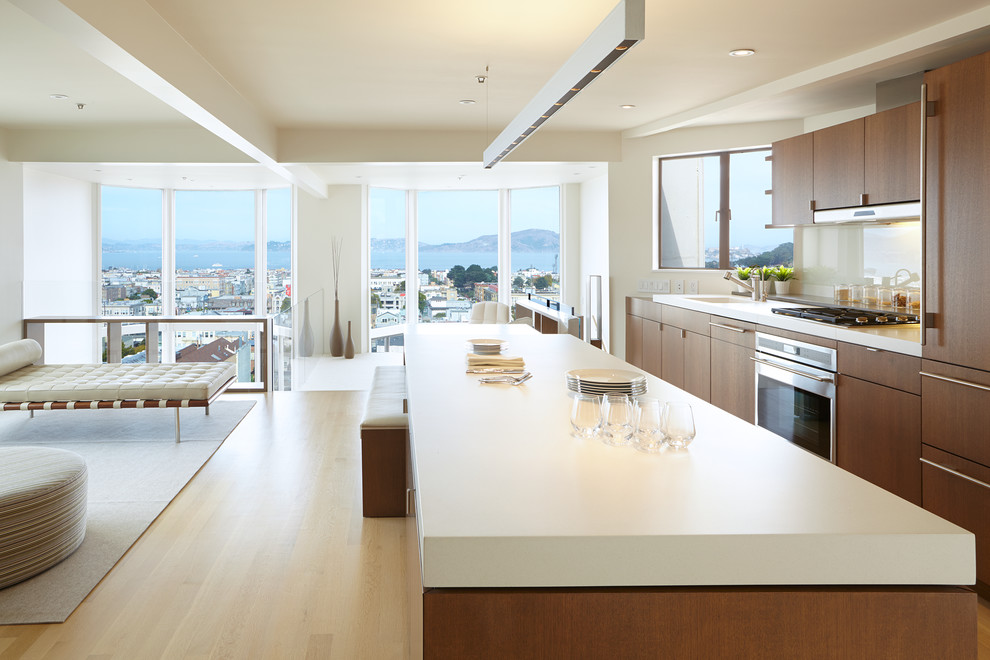 Example of a danish galley light wood floor open concept kitchen design in San Francisco with an integrated sink, flat-panel cabinets, dark wood cabinets, beige backsplash, glass sheet backsplash, stainless steel appliances and an island