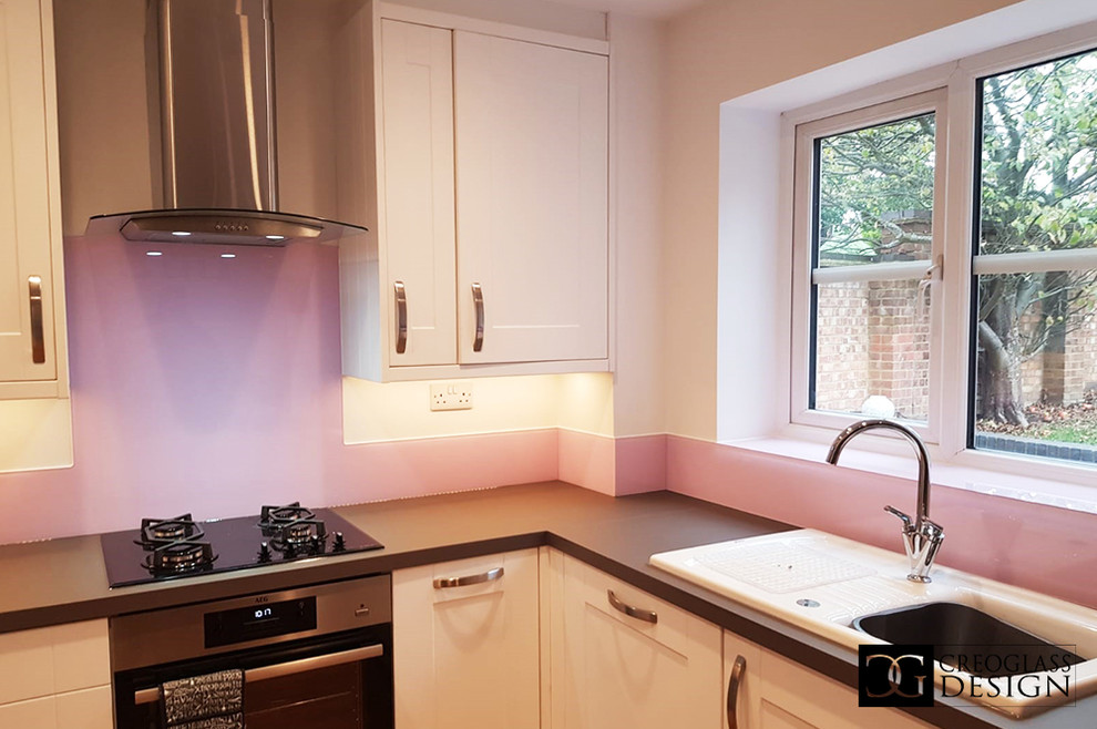 Große Moderne Wohnküche ohne Insel mit weißen Schränken, Küchenrückwand in Rosa, Glasrückwand und grauer Arbeitsplatte in Hertfordshire