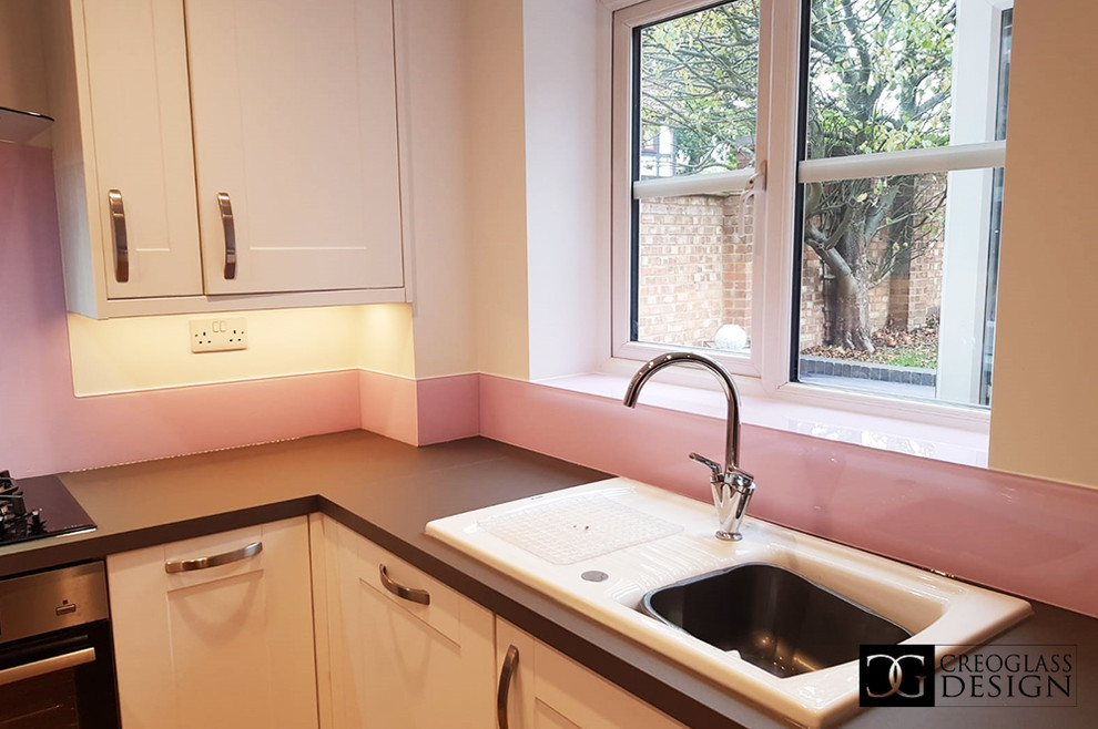 Große Moderne Wohnküche ohne Insel mit weißen Schränken, Küchenrückwand in Rosa, Glasrückwand und grauer Arbeitsplatte in Hertfordshire