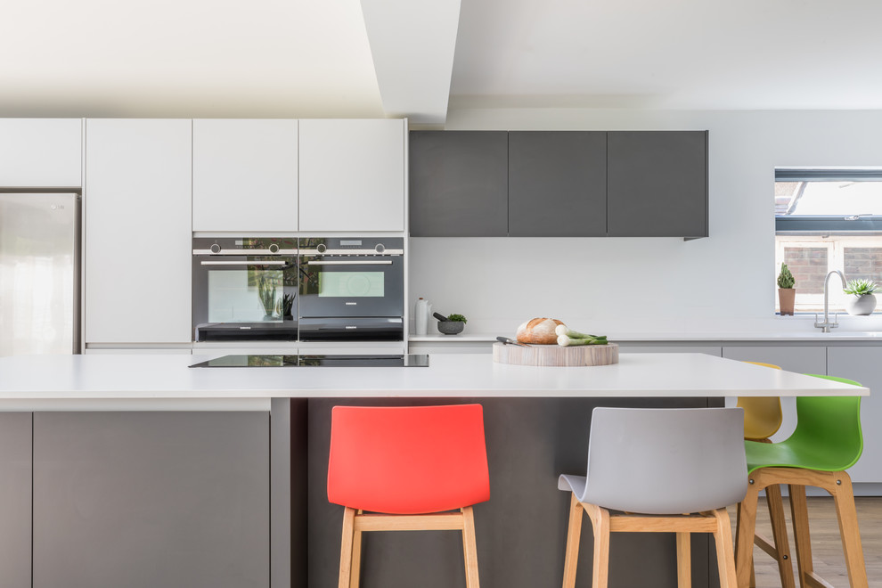 Immagine di una cucina design di medie dimensioni con lavello integrato, ante lisce, ante grigie, top in superficie solida, elettrodomestici in acciaio inossidabile e top bianco