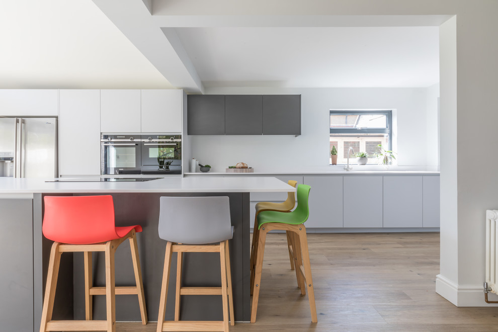 Inspiration for a medium sized contemporary galley kitchen in Sussex with flat-panel cabinets, grey cabinets, composite countertops, stainless steel appliances, an island, white worktops, medium hardwood flooring and brown floors.