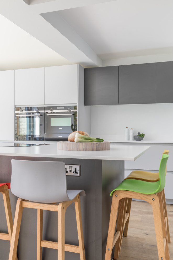 Foto di una cucina minimal di medie dimensioni con lavello integrato, ante lisce, ante grigie, top in superficie solida, elettrodomestici in acciaio inossidabile e top bianco