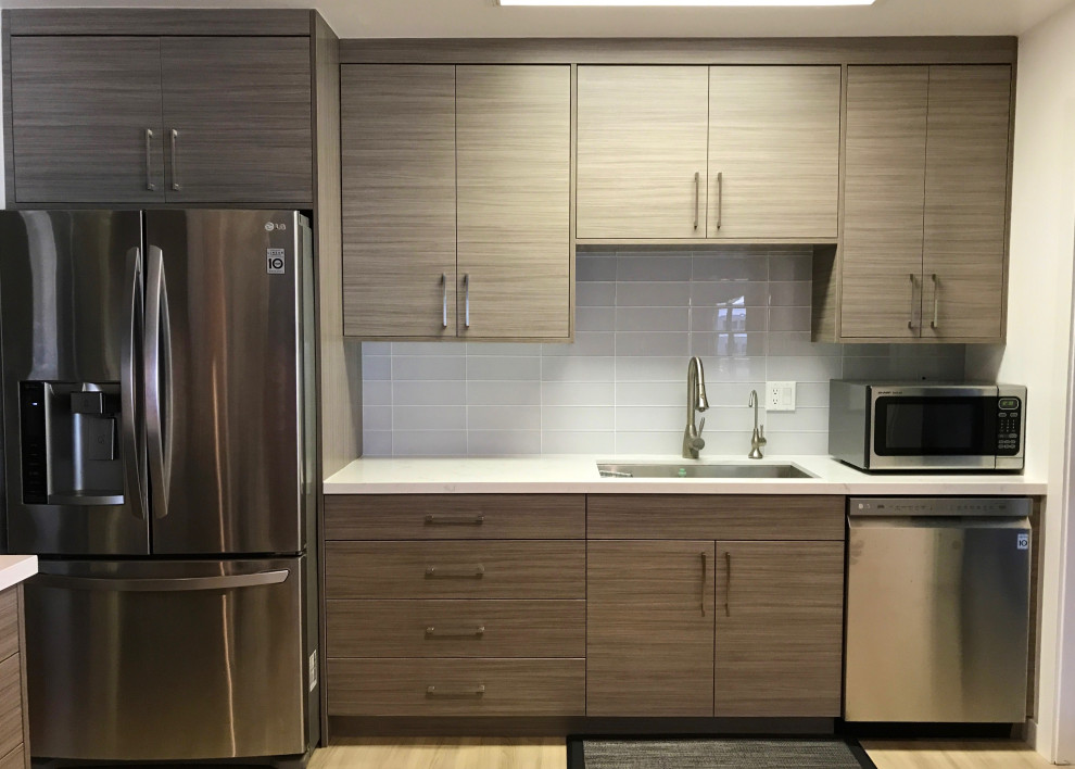 Modelo de cocina moderna con armarios con paneles lisos, puertas de armario de madera oscura, salpicadero de azulejos tipo metro, electrodomésticos de acero inoxidable y encimeras blancas