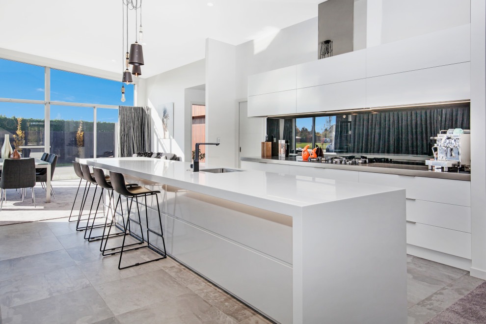 На фото: параллельная кухня-гостиная в современном стиле с врезной мойкой, плоскими фасадами, белыми фасадами, островом, серым полом и серой столешницей с