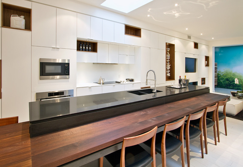 Inspiration for a large modern single-wall kitchen/diner in Toronto with a submerged sink, flat-panel cabinets, white cabinets, white splashback, stainless steel appliances, light hardwood flooring, an island and grey worktops.