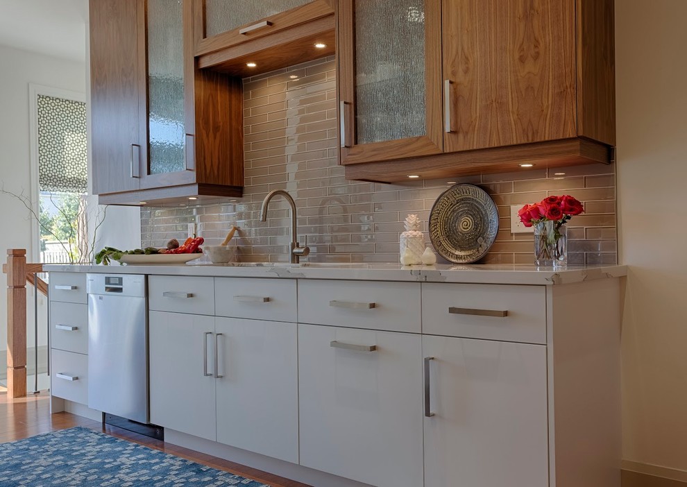 Zweizeilige Moderne Küche mit Triple-Waschtisch, flächenbündigen Schrankfronten, weißen Schränken, Quarzwerkstein-Arbeitsplatte, Küchenrückwand in Grau, Rückwand aus Glasfliesen, Küchengeräten aus Edelstahl, hellem Holzboden und braunem Boden in Toronto