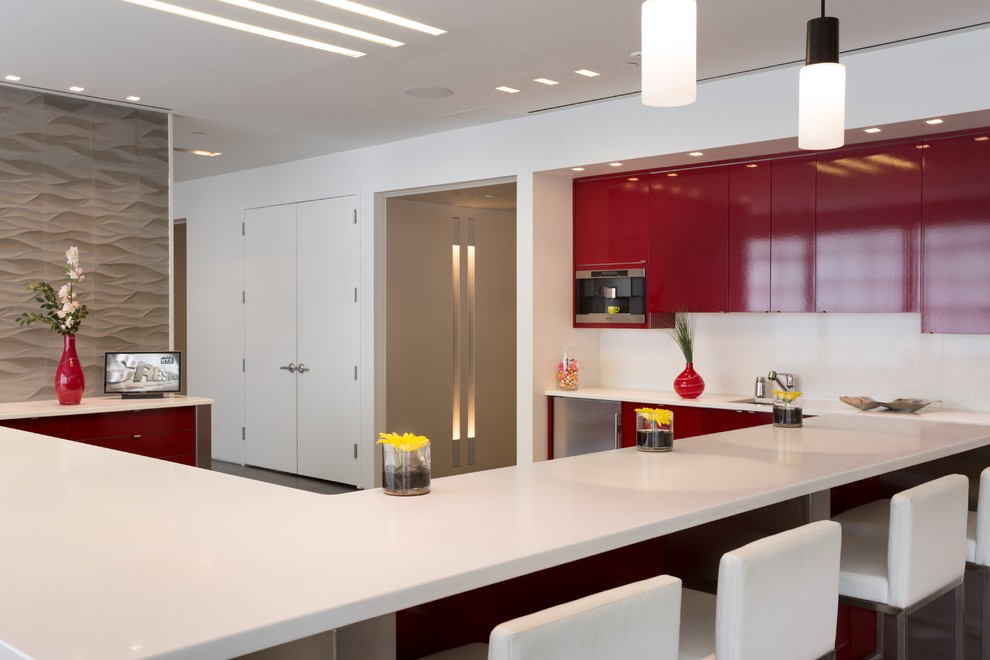 Inspiration for a huge modern u-shaped concrete floor eat-in kitchen remodel in Milwaukee with a drop-in sink, flat-panel cabinets, red cabinets, solid surface countertops, white backsplash, glass sheet backsplash, stainless steel appliances and a peninsula