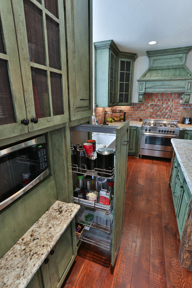 Mittelgroße Stilmix Wohnküche in L-Form mit Landhausspüle, profilierten Schrankfronten, grünen Schränken, Granit-Arbeitsplatte, Küchenrückwand in Rot, Küchengeräten aus Edelstahl, braunem Holzboden und Kücheninsel in Portland