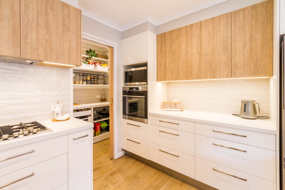 Mid-sized danish u-shaped medium tone wood floor and beige floor open concept kitchen photo in Melbourne with a double-bowl sink, flat-panel cabinets, white cabinets, quartz countertops, white backsplash, porcelain backsplash, stainless steel appliances, a peninsula and white countertops