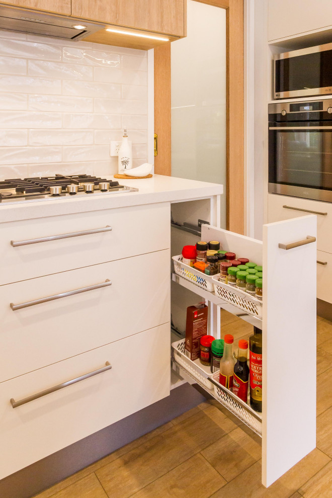 メルボルンにある中くらいな北欧スタイルのおしゃれなキッチン (ダブルシンク、フラットパネル扉のキャビネット、白いキャビネット、クオーツストーンカウンター、白いキッチンパネル、磁器タイルのキッチンパネル、シルバーの調理設備、無垢フローリング、ベージュの床、白いキッチンカウンター) の写真
