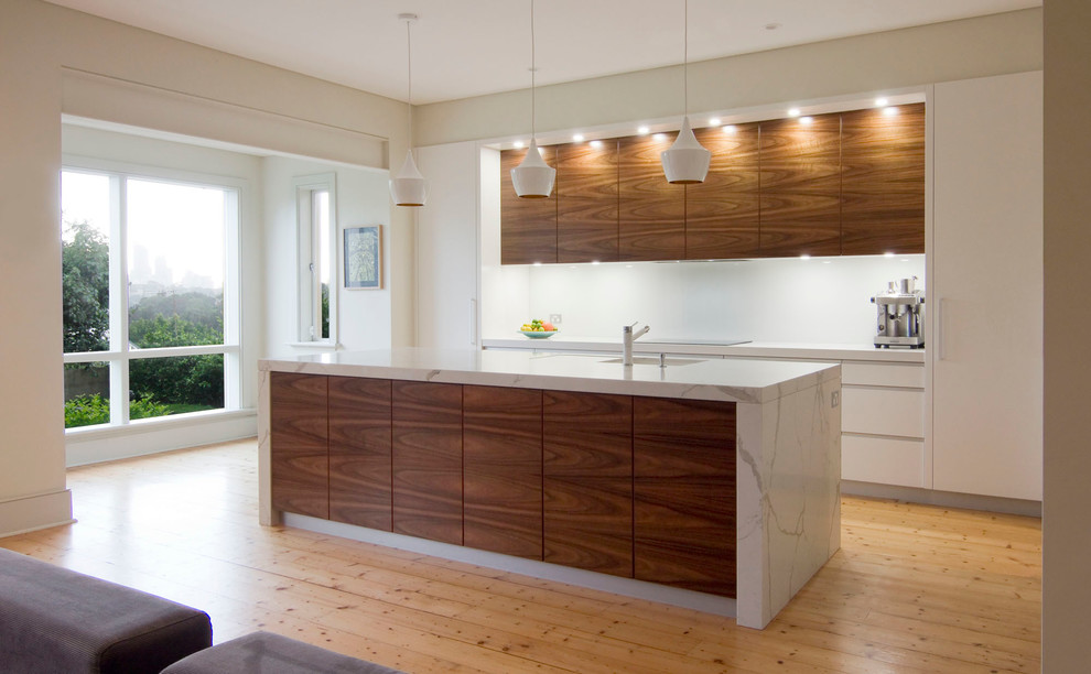 Large modern single-wall open plan kitchen in Sydney with a submerged sink, flat-panel cabinets, engineered stone countertops, white splashback, glass sheet splashback, stainless steel appliances, light hardwood flooring, an island and medium wood cabinets.