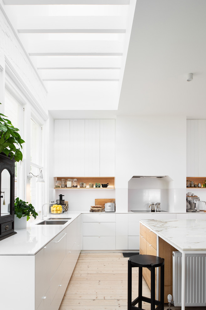 Inspiration for a large beach style l-shaped open plan kitchen in Hobart with a submerged sink, flat-panel cabinets, white cabinets, white splashback, light hardwood flooring, an island, beige floors, white worktops, marble worktops and white appliances.