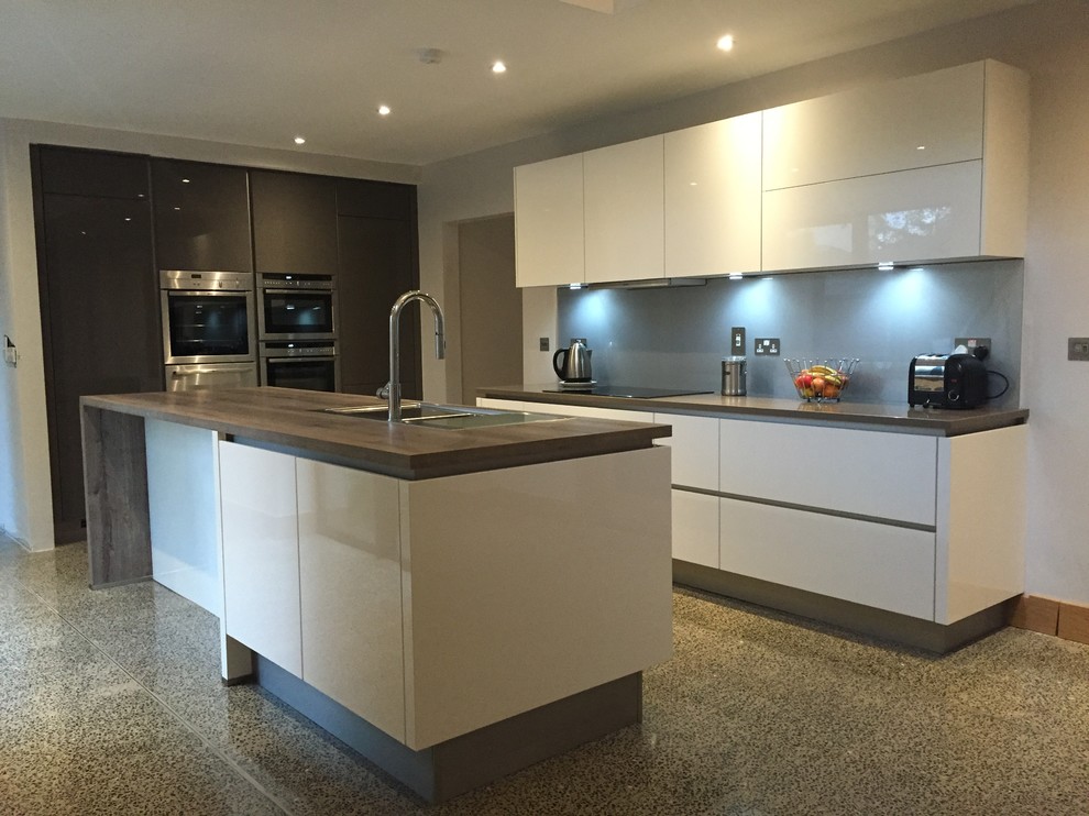 This is an example of a medium sized contemporary kitchen/diner in Limerick with a built-in sink, flat-panel cabinets, grey cabinets, quartz worktops, metallic splashback, glass sheet splashback, stainless steel appliances, concrete flooring and an island.
