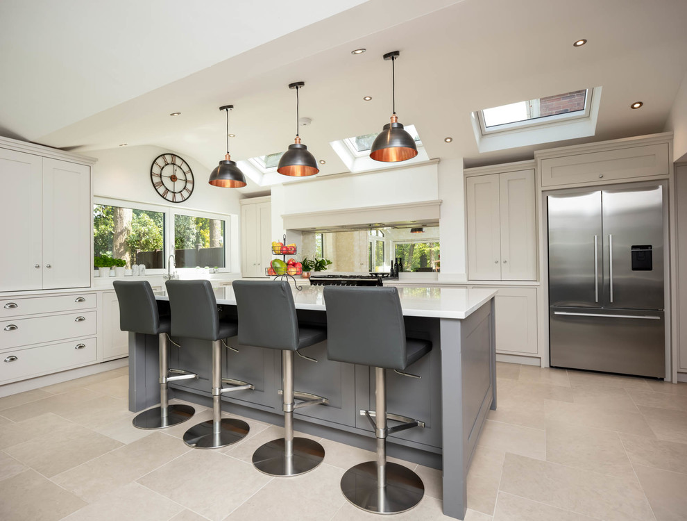 Photo of a medium sized classic kitchen in Berkshire with shaker cabinets, beige cabinets, mirror splashback, stainless steel appliances, an island, beige floors and white worktops.